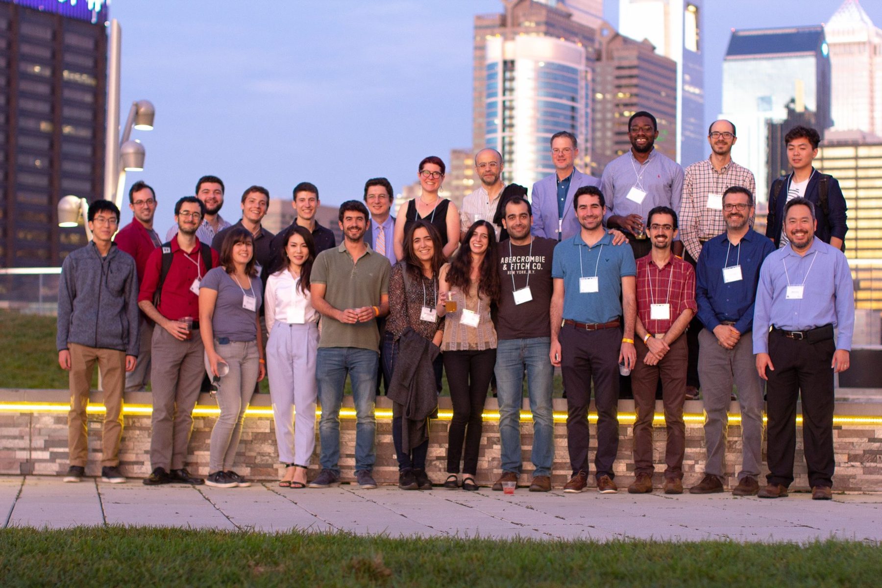 Alumni of the Pappas research group on a rooftop terrace at dusk, with the Philadelphia skyline behind them